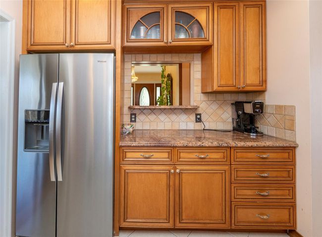 Kitchen with brown cabinetry, backsplash, light stone counters, and stainless steel fridge | Image 22