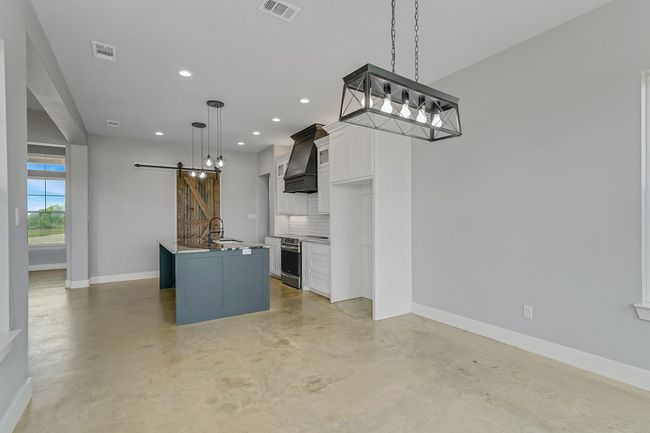 Kitchen featuring a barn door, tasteful backsplash, concrete floors, baseboards, and premium range hood | Image 11