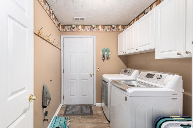 Clothes washing area with cabinet space, washing machine and clothes dryer, wood finished floors, a textured ceiling, and baseboards | Image 32