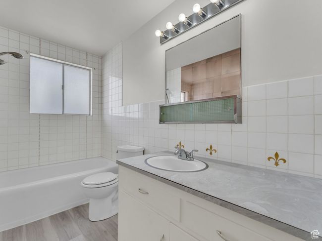 Full bath with wood finished floors, bathing tub / shower combination, tile walls, toilet, and vanity | Image 9