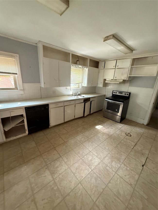 Kitchen featuring dishwashing machine, stove, open shelves, ventilation hood, and light countertops | Image 12