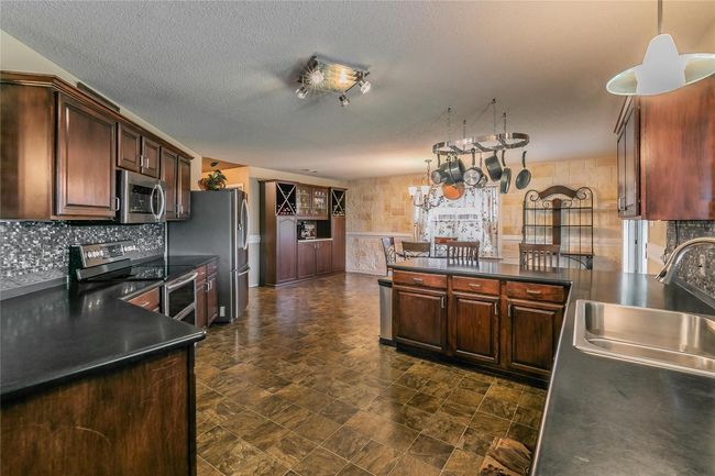 Kitchen with appliances with stainless steel finishes, a chandelier, dark countertops, a peninsula, and decorative light fixtures | Image 6