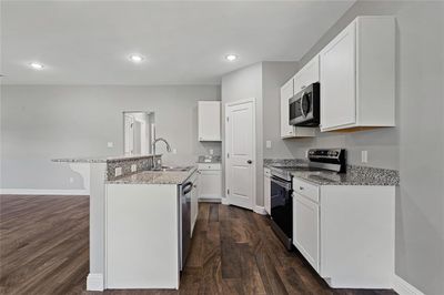 Kitchen featuring dark hardwood / wood-style floors, appliances with stainless steel finishes, a kitchen island with sink, sink, and white cabinets | Image 2