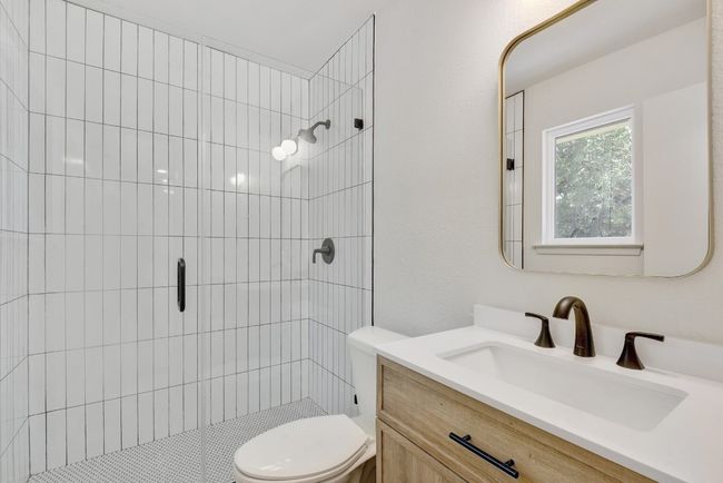Your ensuite bathroom has been completely updated and includes including a walk-in shower with a frameless glass door that encases white, linear subway tile and penny mosaic tile in the shower drain, modern matte black hardware and fixtures, hexagonal matte porcelain floor tile, and a natural oak finish vanity. | Image 15