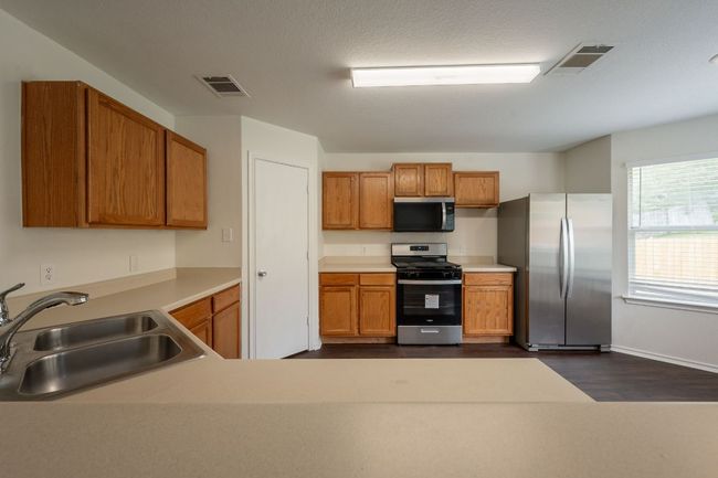 Kitchen with stainless steel appliances, a sink, brown cabinetry, light countertops, and dark wood-type flooring | Image 9