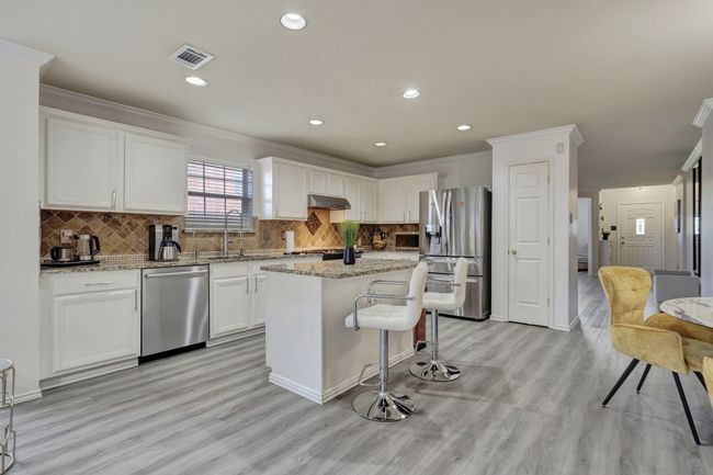 Kitchen with backsplash, white cabinetry, light stone counters, a center island, and stainless steel appliances | Image 13