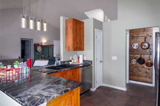 Kitchen featuring a peninsula, brown cabinetry, dark stone counters, dishwasher, and a sink | Image 41