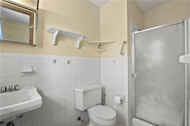 Bathroom featuring tile walls, a sink, a stall shower, toilet, and wainscoting | Image 18