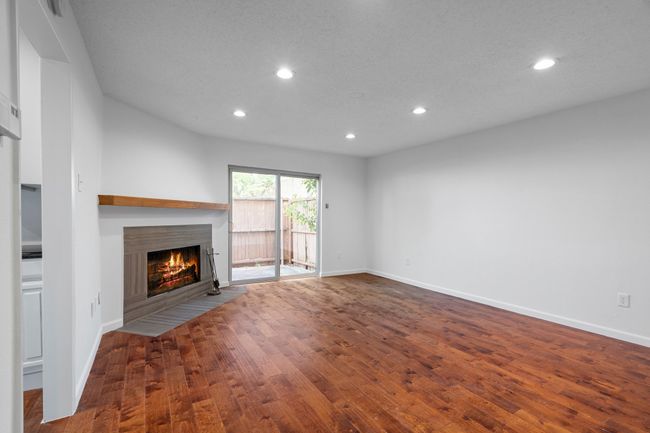 Living room with a fireplace with flush hearth, wood finished floors, sliding door, and recessed lighting | Image 7