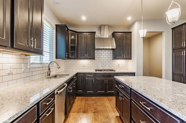 kitchen featuring wall chimney range hood, a sink, light wood-style floors, appliances with stainless steel finishes, and light stone countertops | Image 19