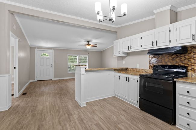 Kitchen featuring black electric range, under cabinet range hood, light wood-style floors, a peninsula, and white cabinets | Image 20