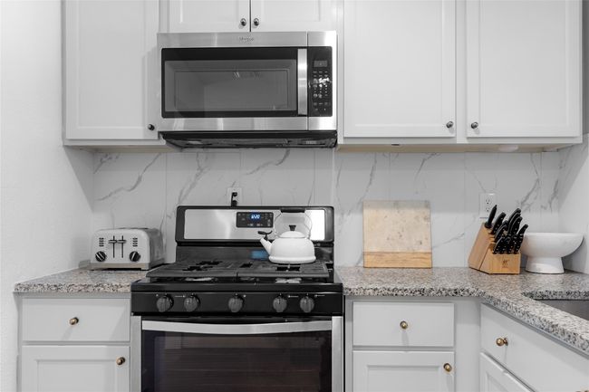 Kitchen featuring gas range, light stone countertops, white cabinets, and backsplash | Image 12