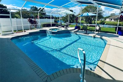 This beautiful screened-in pool area offers a resort-like setting with a sparkling pool and an elevated spillover spa, perfect for relaxation and entertainment. The pool’s design features a spacious deck with ample room for lounging and dining, while the raised spa cascades into the pool, creating a soothing waterfall effect. Beyond the pool, enjoy a tranquil view of the nearby pond, providing a peaceful backdrop to this outdoor oasis. The surrounding landscaping and privacy screens add an extra layer of seclusion. In the evenings, string lights around the enclosure create a warm and inviting ambiance, transforming the space into a serene retreat under the stars. This outdoor area is ideal for both daytime enjoyment and evening relaxation, combining elegance with a touch of nature. | Image 2