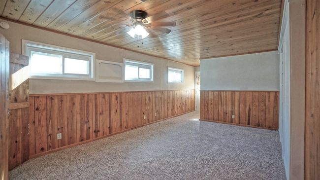 Unfurnished room featuring wooden ceiling, a wainscoted wall, wood walls, ceiling fan, and carpet flooring | Image 9