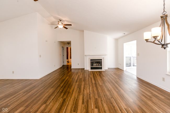 unfurnished living room featuring a fireplace with flush hearth, dark wood-style flooring, baseboards, lofted ceiling, and ceiling fan with notable chandelier | Image 5