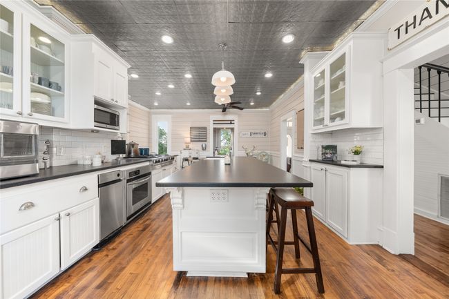 Kitchen featuring dark countertops, stainless steel appliances, white cabinets, backsplash, and a center island, ceiling tin tiles | Image 7