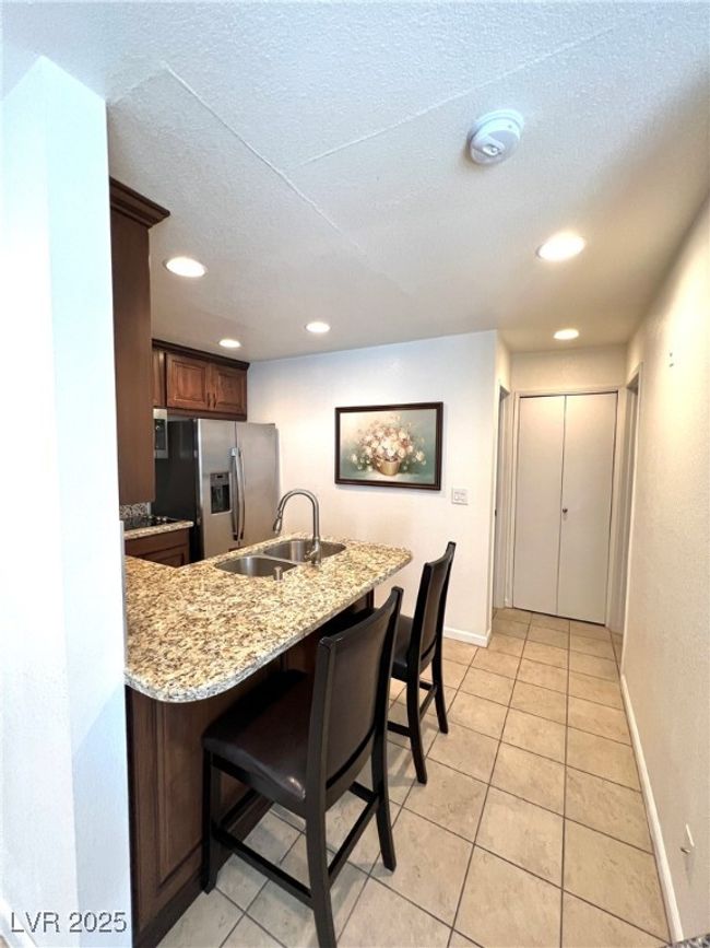 Kitchen with a kitchen bar, stainless steel refrigerator with ice dispenser, a sink, light stone counters, and a peninsula | Image 22