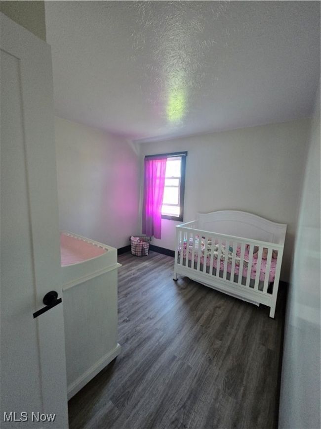 Bedroom with wood finished floors, a textured ceiling, a crib, and baseboards | Image 24