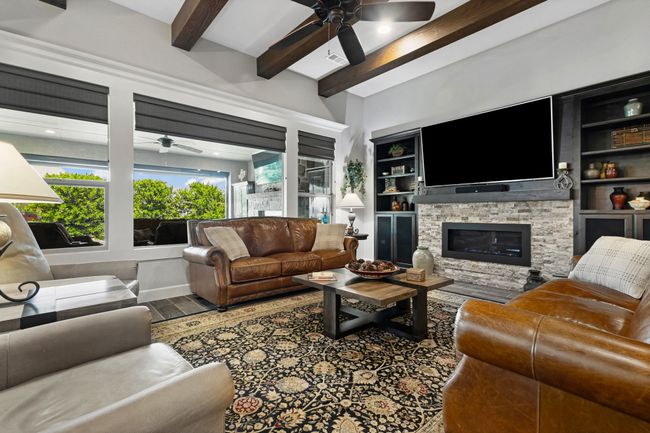 Living room with ceiling fan, beam ceiling, a fireplace, wood finished floors, and built in features | Image 7