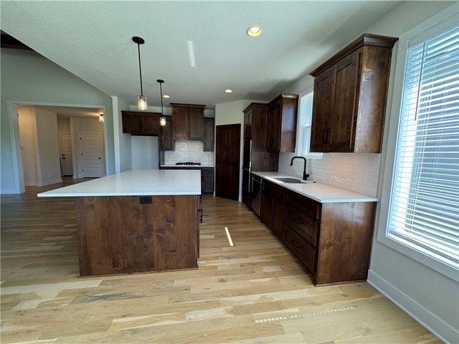 Kitchen featuring light wood-style floors, a kitchen island, dark brown cabinets, tasteful backsplash, and pendant lighting | Image 20