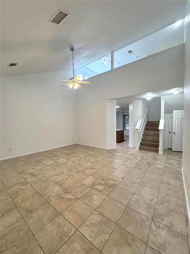 Unfurnished living room with a ceiling fan, high vaulted ceiling, stairway, and light tile patterned floors | Image 4