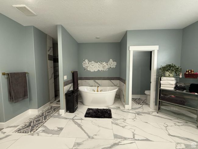 Full bath featuring a textured ceiling, visible vents, marble finish floor, toilet, and a freestanding bath | Image 42