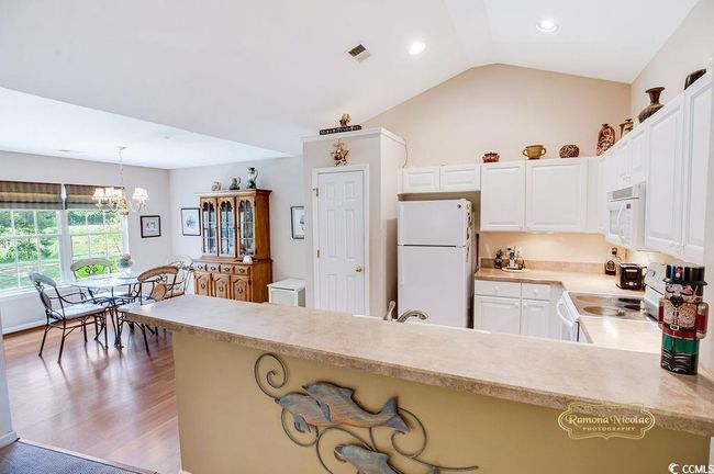 Kitchen featuring white appliances, light countertops, a chandelier, decorative light fixtures, and white cabinetry | Image 16