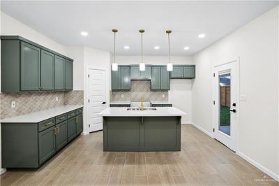 Kitchen featuring tasteful backsplash, sink, light hardwood / wood-style floors, hanging light fixtures, and green cabinets | Image 2