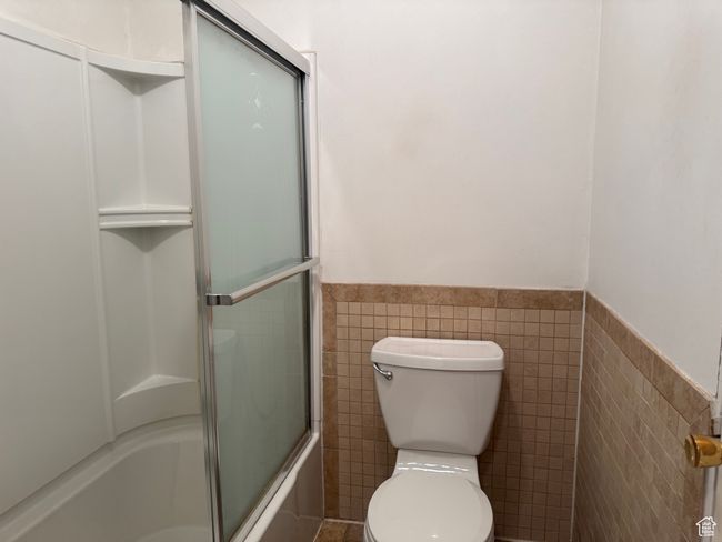 Full bath featuring tile walls, a wainscoted wall, bath / shower combo with glass door, and toilet | Image 25