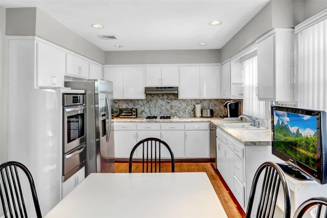 Kitchen featuring sink, appliances with stainless steel finishes, light hardwood / wood-style floors, decorative backsplash, and white cabinets | Image 12