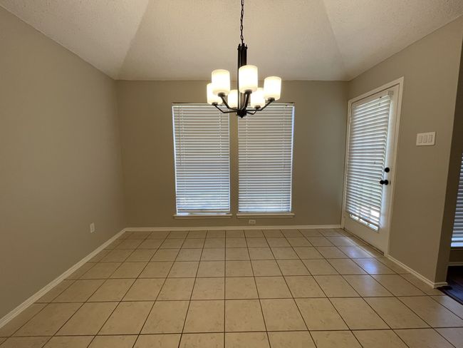 Empty room with a chandelier, light tile patterned floors, a textured ceiling, and lofted ceiling | Image 5