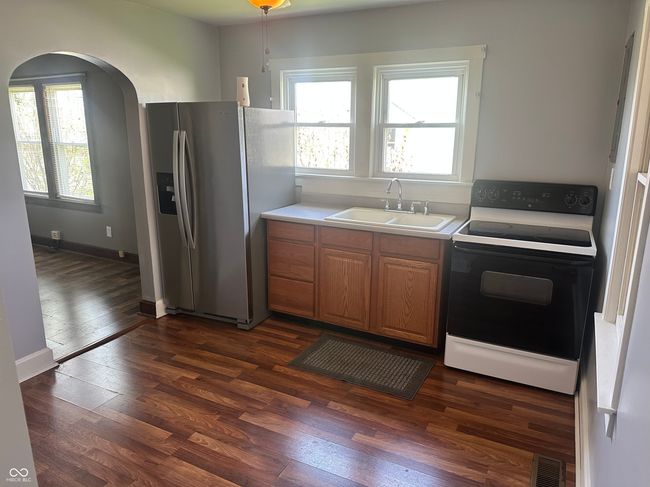 kitchen featuring dark wood-style floors, a sink, electric range oven, stainless steel refrigerator with ice dispenser, and visible vents | Image 5
