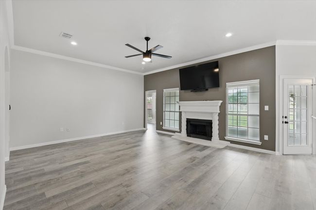 Unfurnished living room featuring a ceiling fan, baseboards, a fireplace with raised hearth, wood finished floors, and ornamental molding | Image 5