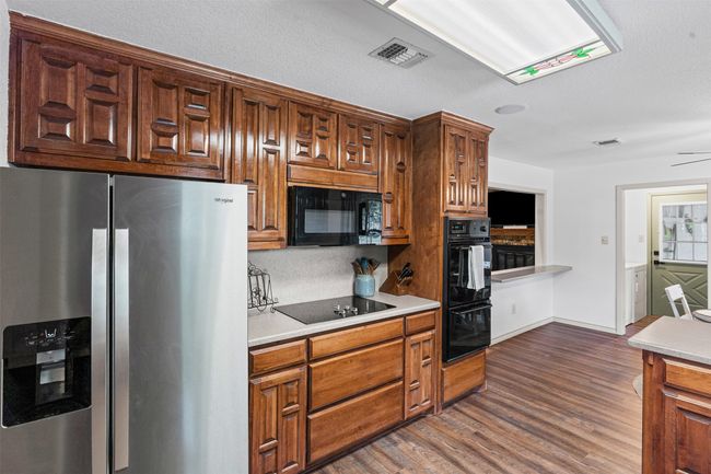 Kitchen with black appliances, dark wood-style flooring, light countertops, and brown cabinets | Image 13
