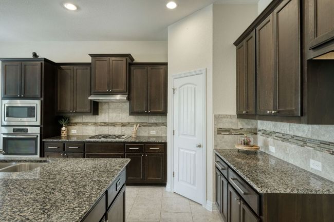 Kitchen featuring dark granite countertops, decorative backsplash, appliances with stainless steel finishes, and under cabinet range hood | Image 10