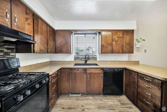 Kitchen featuring black appliances, a sink, under cabinet range hood, light wood finished floors, and light countertops | Image 13