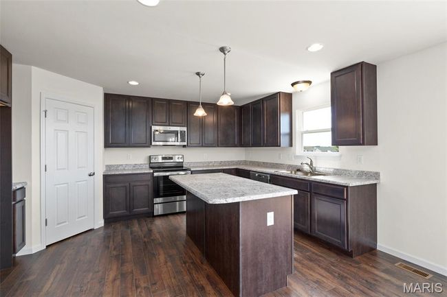 Kitchen featuring stainless steel appliances, dark brown cabinetry, light countertops, dark wood-type flooring, and a kitchen island | Image 6