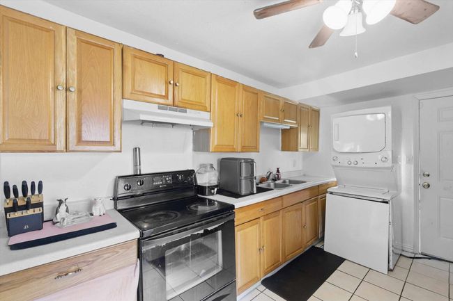 Kitchen featuring a sink, light countertops, stacked washer / dryer, black / electric stove, and under cabinet range hood | Image 8
