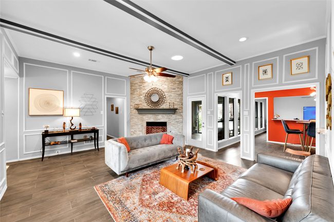 Living area with a decorative wall, ceiling fan, beam ceiling, wood finished floors, and a stone fireplace | Image 9
