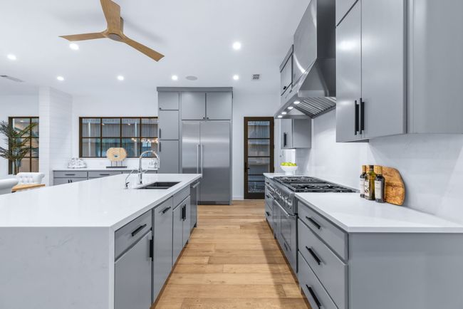 Kitchen with gray cabinetry, wall chimney exhaust hood, premium appliances, ceiling fan, and light wood-type flooring | Image 7