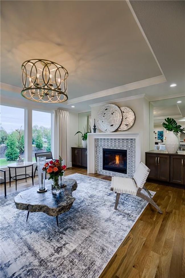 Living room with wood-type flooring, a tray ceiling, a tile fireplace, an inviting chandelier, and ornamental molding | Image 5