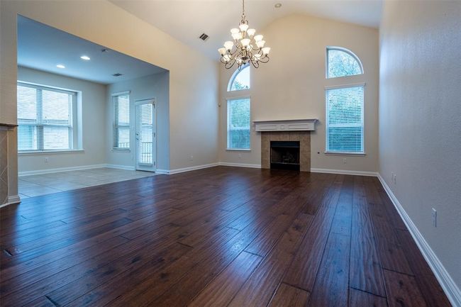 Unfurnished living room featuring a tiled fireplace, a chandelier, wood-type flooring, plenty of natural light, and lofted ceiling | Image 5