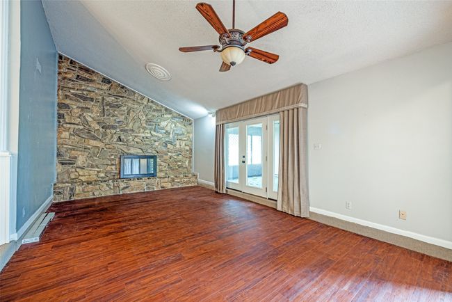 Unfurnished living room with a ceiling fan, a fireplace, wood finished floors, a textured ceiling, and baseboards | Image 4