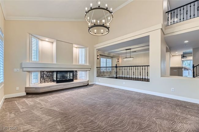 Unfurnished living room featuring a chandelier, crown molding, carpet floors, a high ceiling, and a fireplace | Image 4