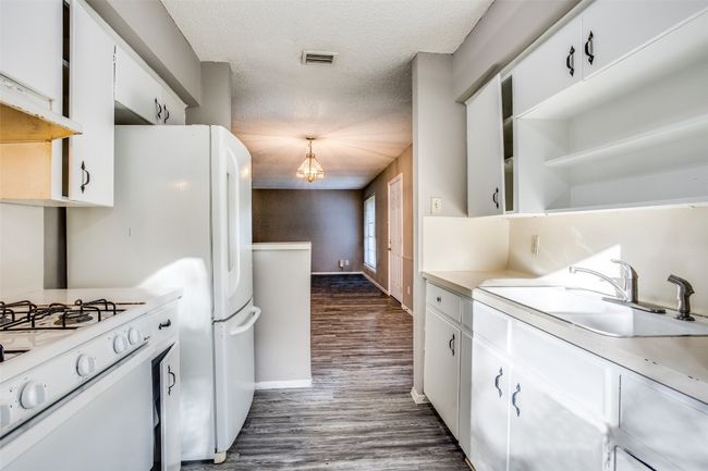 Kitchen featuring visible vents, white appliances, baseboards, dark wood-type flooring, and white cabinetry | Image 12