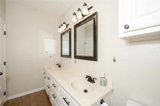 Full bathroom featuring a sink, double vanity, baseboards, toilet, and wood finished floors | Image 22