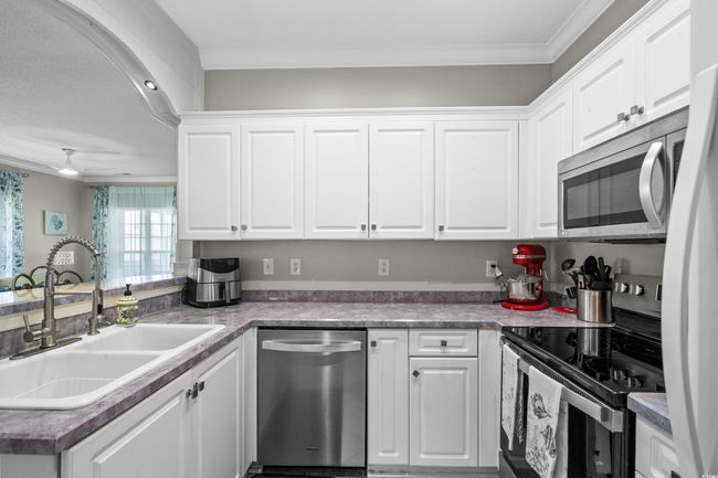 Kitchen featuring stainless steel appliances, a sink, white cabinets, a peninsula, and ornamental molding | Image 17