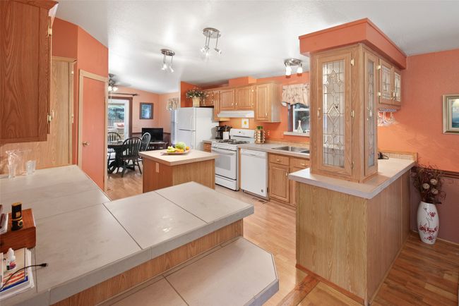 Kitchen with white appliances, light wood-style floors, a kitchen island, under cabinet range hood, and light countertops | Image 14