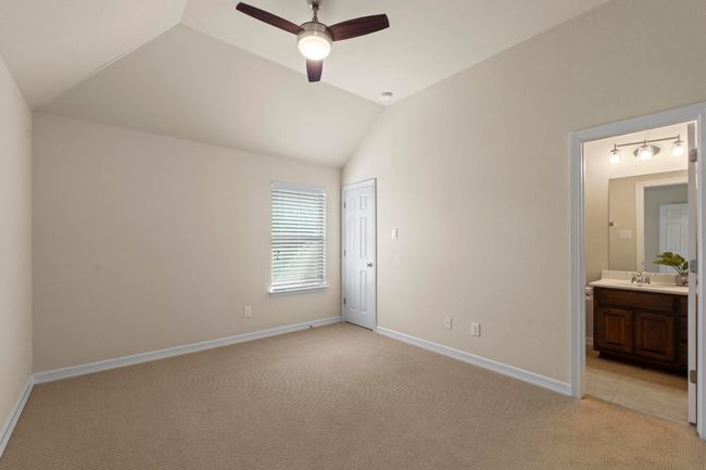 Unfurnished bedroom with light colored carpet, lofted ceiling, connected bathroom, a closet, and ceiling fan | Image 29