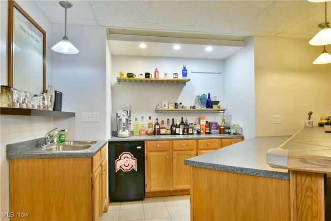 Indoor wet bar with dishwasher, light tile patterned floors, a paneled ceiling, and decorative light fixtures | Image 40